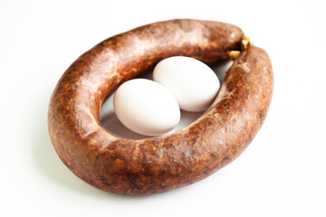 Homemade coiled sausage made of various spice mixes used in Turkish cuisine and two eggs, isolated on white background