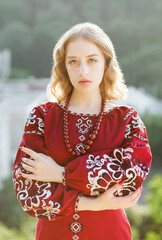 Portrait of a young blonde in a red national dress posing outdoors.