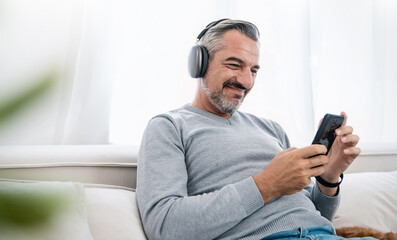 Portrait of senior old caucasian man stay home sit on the sofa living room listen to music head...