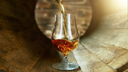 Pouring rum into glass inside old wooden barrel.