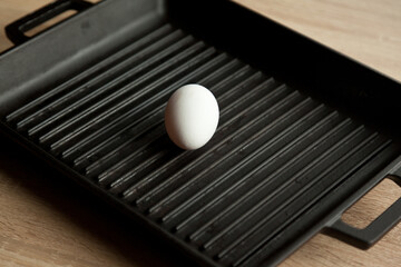 Black cast heavy iron grill pan in organic white eggs; on modern oak kitchen countertop