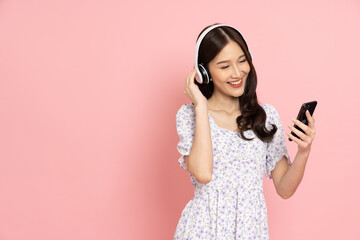 Beautiful and happy asian woman in a dress is listening to her phone through her headphones with a...