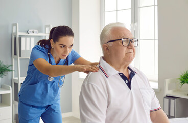 Female chiropractor or physiotherapist examining a senior male patient with spine problems and back...