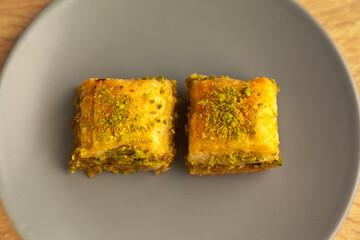 Baklava with pistachio, one of the most beautiful desserts of Turkish cuisine, in gray plate, on oak cutting board