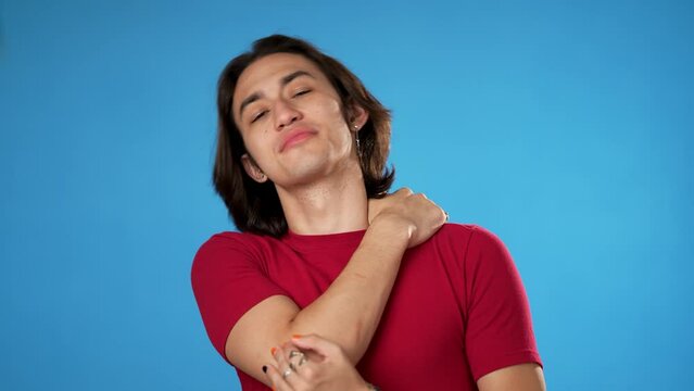 Portrait of Latino Hispanic gender fluid young hipster man 20s with sore neck shoulder problem isolated on blue background in studio