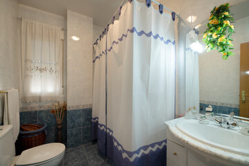 Bathroom with marble countertop and sink, mirror in furniture and bathtub with PVC curtain and blue and white tiled border