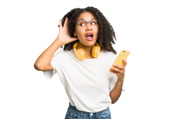 Young african american woman listening to music with yellow headphones isolated trying to listening a gossip.