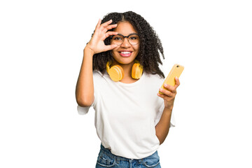 Young african american woman listening to music with yellow headphones isolated excited keeping ok...