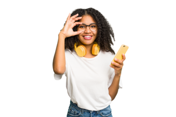 Young african american woman listening to music with yellow headphones isolated excited keeping ok gesture on eye.