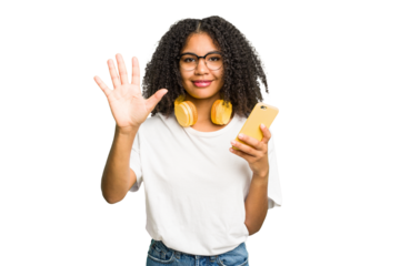Young african american woman listening to music with yellow headphones isolated smiling cheerful showing number five with fingers.