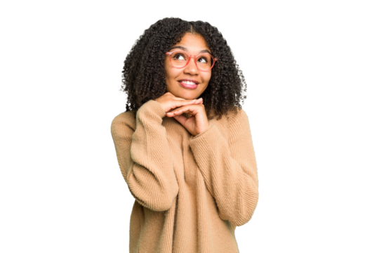 Young african american woman isolated keeps hands under chin, is looking happily aside.