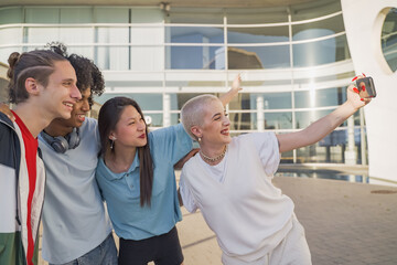 Multiethnic teenage friends taking a selfie group photo and laughing happy in the campus. Technology lifestyle concept.