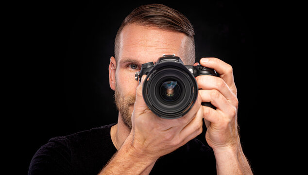 A man with a beard takes pictures with a camera on a dark background.