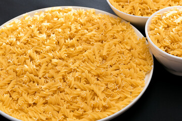 Uncooked Fusilli Pasta Lying on White Plate on Black Background. Raw and Dry Macaroni. Unhealthy and Fat Food