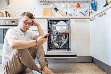 man in a smartphone looks at the instructions for the dishwasher in the kitchen.