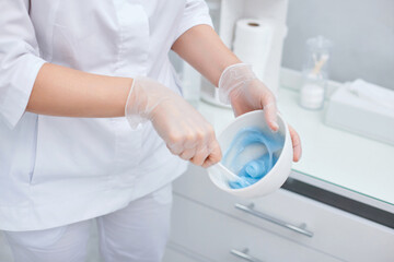 bowl with blue alginate mask in hands of beautician.