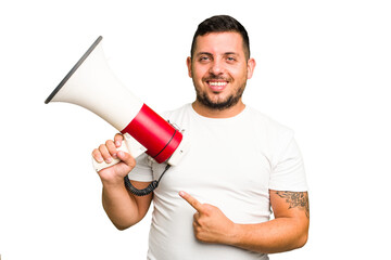 Young caucasian man holding a megaphone isolated smiling and pointing aside, showing something at blank space.