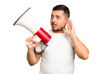 Young caucasian man holding a megaphone isolated trying to listening a gossip.