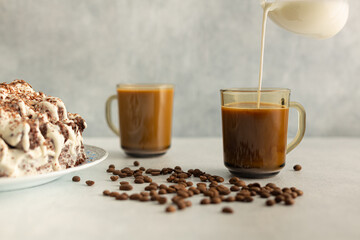 Coffee with cream in a glass mug with coffee beans, cream cake. cream is poured from a glass jug. Drink on a light gray background.