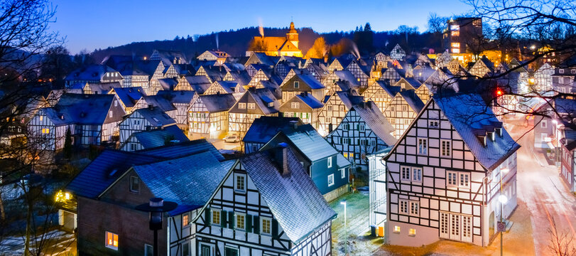 Winter panorama of Freudenberg in Sauerland Germany at blue hour twilight. Historic old town in rural scenery with half timbered black and white facades on cold snowy winter evening at christmas time.