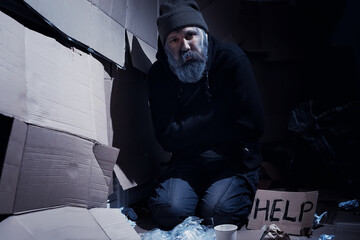 A homeless bearded man sits on boxes on the street and asks for help. Need a homeless person asks for money for food and overnight.