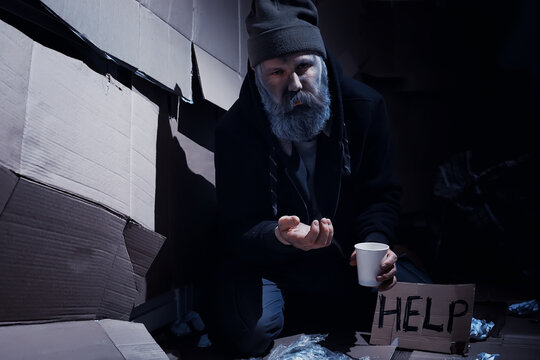 A homeless bearded man sits on boxes on the street and asks for help. Need a homeless person asks for money for food and overnight.