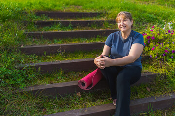 Standing and holding yoga mat. Senior woman having nice weekend outdoors on the field at sunny day.