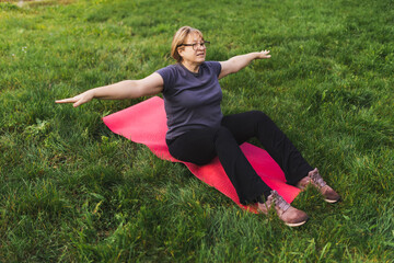 Mature caucasian retired woman in the park meditates and performs breathing exercises, summer day
