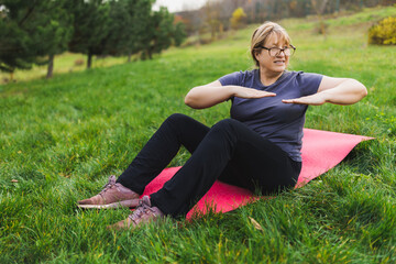 Mature caucasian retired woman in the park meditates and performs breathing exercises, summer day