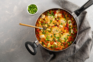 Shakshuka in a frying pan with tomatoes in vegetable sauce with cheese. A dish of fried eggs in a sauce of tomatoes, pepper, onion, garlic and seasonings Horizontal orientation, copy space, top view