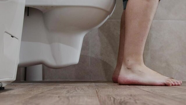 A man puts on denim shorts in the toilet after having a bowel movement. Koznept prolonged sitting on the toilet. Health of the intestines and digestive tract, hemorrhoids.