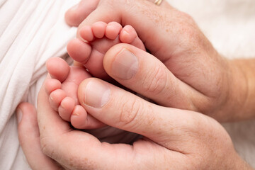 Mother and father are doing massage on her baby foot. Closeup baby feet in mother hands. Prevention of flat feet, development, muscle tone, dysplasia. Family, love, care, and health concepts.