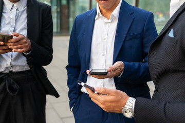 Crop multiethnic colleagues using smartphones together
