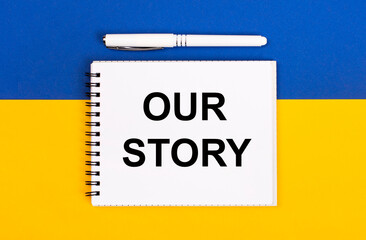 Obraz premium A white notebook with the text OUR STORY and a white pen on a blue and yellow background.