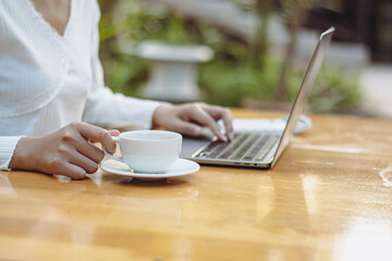 woman in white shirt holding coffee cup and typing on laptop