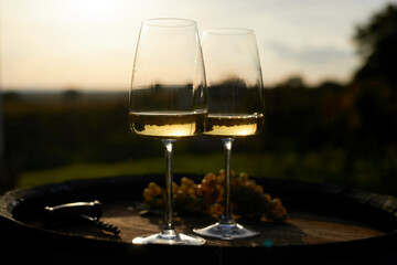 Close-up of two glasses of white wine with corkscrew and grapes on a wooden barrel after sunset