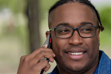Friendly young man with glasses talks on a cell phone, arranges a meeting with friends. Portrait of a man with a close-up of an African hairstyle and a phone in his hand