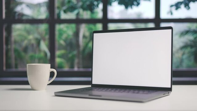 Workplace with laptop and cup of coffee, desktop computer with blank white screen of copy space, window and trees view