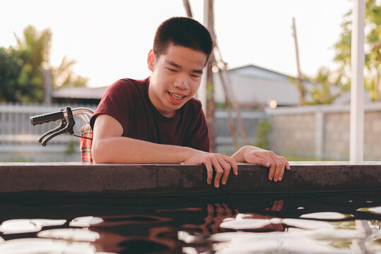 Teenager boy with a disability looking and feeding fish in pond with smile and happy face, Training of muscles through picking,Animals therapy,Outdoor ativity,Rehabilitation and Mental Health concept.