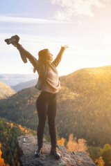 a woman photographer with a camera on top of a mountain, threw her arms to the sides, rejoices in the beautiful nature and freedom. Nature photography landscape photographer