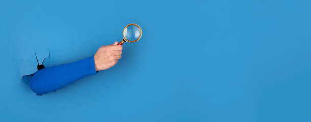magnifier in hand over blue background, search concept, panoramic layout