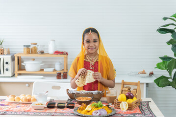 Indian girl, 8-year-old, wearing a red sari, standing in the kitchen and eating Indian food. to people and food culture concept.