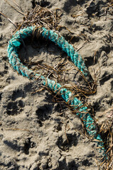 Un pezzo di corda verde parzialmewnte sepolto dalla sabbia su una spiaggia - obrazy, fototapety, plakaty