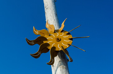 Una girandola a forma di sole appesa ad un tronco di legno sulla spiaggia si staglia sul cielo...