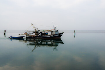 Un peschereccio naviga nelle acque tranquille della laguna di Venezia davanti all'isola di Pellestrina in una nuvolosa giornata invernale 