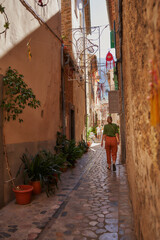 Fototapeta na wymiar Mujer de espaldas camina en una calle de colores cálidos de un pueblo pintoresco en el Mediterráneo