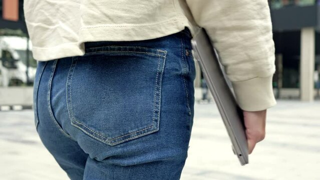Woman in jeans with a laptop in her hands walks along the city street.