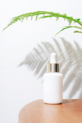 White serum bottle on a background of white wall with fern leaf shadow. Natural skincare products concept