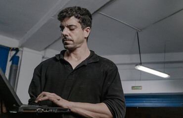 Car mechanic working on laptop in workshop