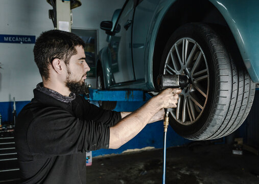 Mechanic with screwdriver repairing car wheel in workshop